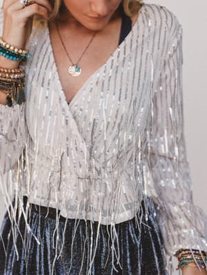 Person wearing a sparkly silver top with fringe details.