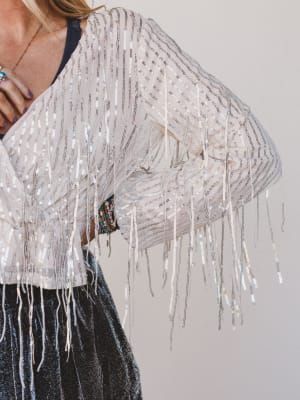 Person wearing a white fringe top with a plain background