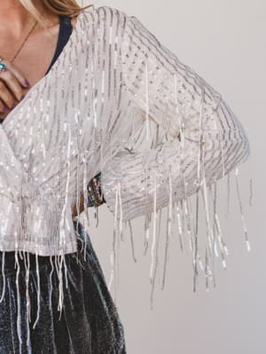 Person wearing a white fringe top with a plain background