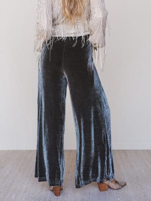 Person wearing dark blue velvet pants with a white top and fringe details.
