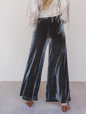 Person wearing black velvet wide-leg pants with a white top and fringe details.