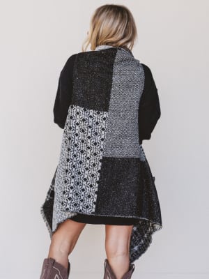 Person wearing a black and gray patterned vest with a plain background