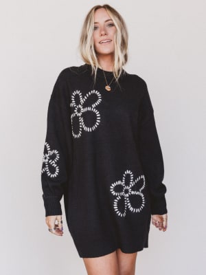 Person wearing a black sweater dress with white patterns on a plain background