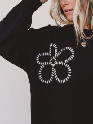 Black sweater with white geometric design worn by a person on a light gray background