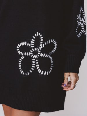 Black sweater with white floral pattern held by a person against a neutral background