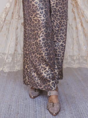 Leopard print pants with a white lace garment and metallic shoes on a textured surface.