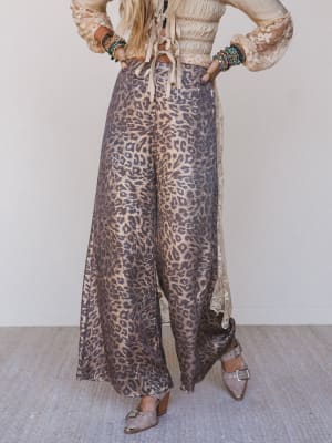 Person wearing leopard print pants and a light-colored top with ruffled sleeves against a neutral background.