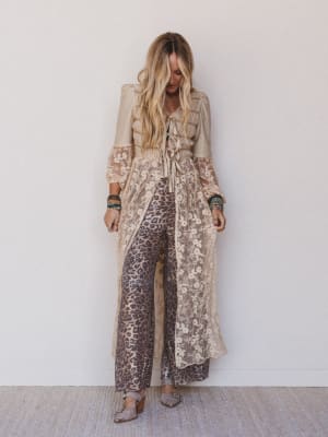 Woman wearing a floral dress over leopard print pants against a white wall