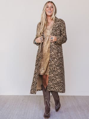 Woman wearing a leopard print coat and boots against a plain background