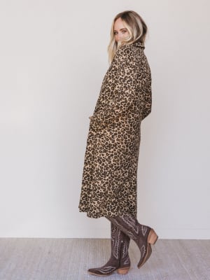Person wearing a leopard print dress and brown boots against a white background