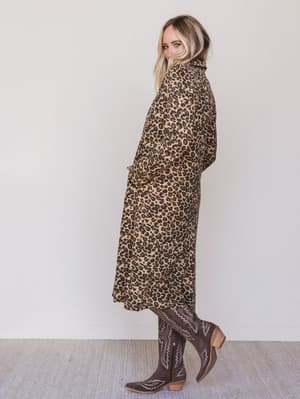 Person wearing a leopard print dress and brown boots against a white background