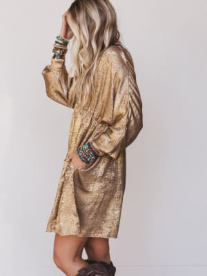 Woman wearing a gold metallic dress with colorful bracelets on a plain background