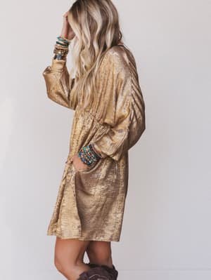 Woman wearing a gold metallic dress with colorful bracelets on a plain background