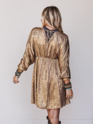 Woman wearing a gold metallic dress with long sleeves against a plain background