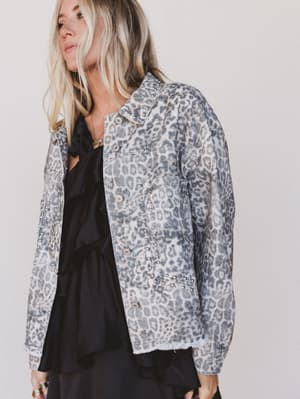 Person wearing a leopard print jacket over a black outfit on a plain background
