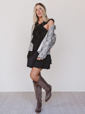 Woman wearing a black dress with a patterned jacket and brown boots against a white background