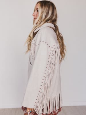 Woman wearing a beige fringe sweater against a white background