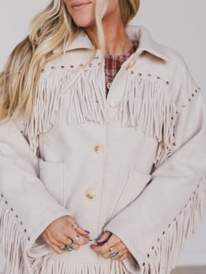 Person wearing a beige fringed jacket with a neutral background
