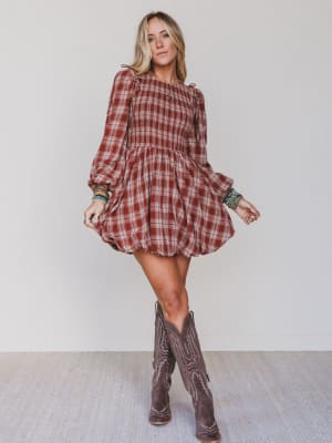 Woman wearing a plaid dress and cowboy boots against a plain background