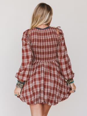 Person wearing a plaid dress with long sleeves on a plain background