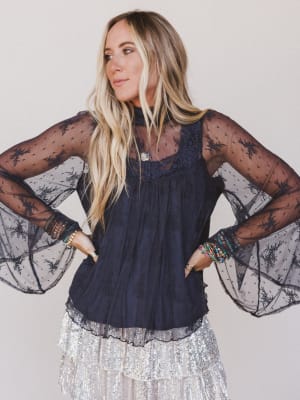 Woman wearing a dark blue top with sheer sleeves against a plain background