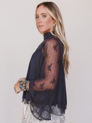 Woman wearing a dark blue sheer top with lace details on a plain background