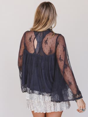 Back view of a person wearing a sheer dark blue lace top with long sleeves on a plain background