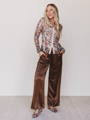 Woman wearing a floral blouse and brown velvet pants against a white background