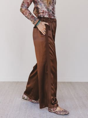 Person wearing a floral top and brown satin pants on a plain background