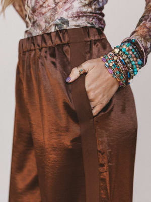 Person wearing brown pants with a colorful bracelet on a plain background