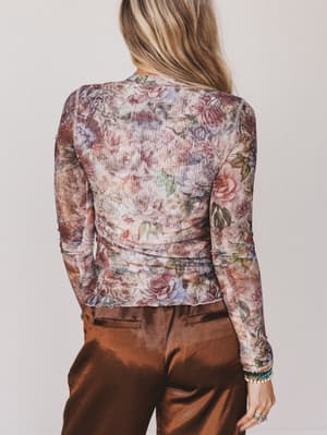 Person wearing a floral long-sleeve top and brown pants against a plain background