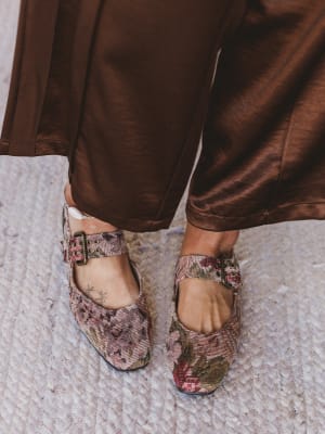 Floral-patterned shoes worn with brown satin pants on a textured surface