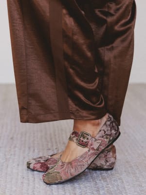 Person wearing floral shoes with a brown satin skirt on a neutral background