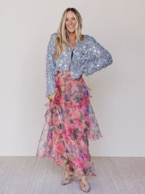 Woman wearing a sequin jacket and floral dress against a white background