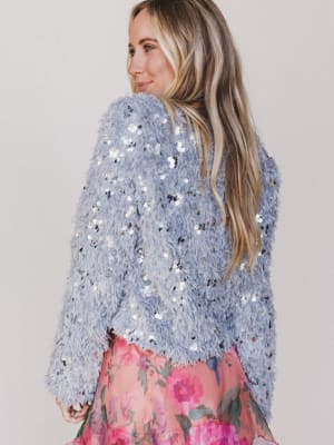 Woman wearing a sequined top and floral skirt against a plain background