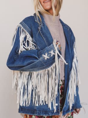 Person wearing a blue denim jacket with white fringe on a plain background