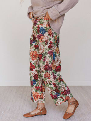 Person wearing floral pants and a beige sweater on a plain background