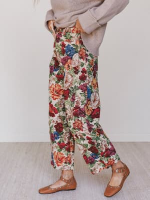 Person wearing floral pants and a beige sweater on a plain background