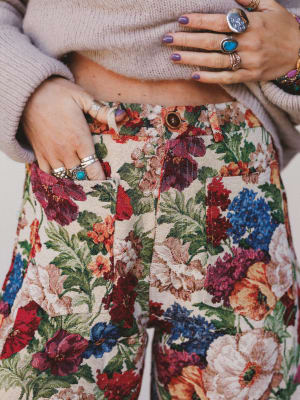 Person wearing floral pants with colorful rings on fingers