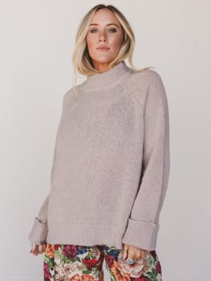 Woman wearing a light gray sweater with floral pants on a plain background