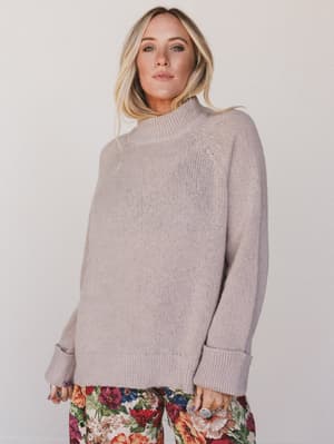 Woman wearing a light gray sweater with floral pants on a plain background