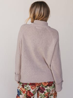 Person wearing a beige sweater and floral pants against a plain background