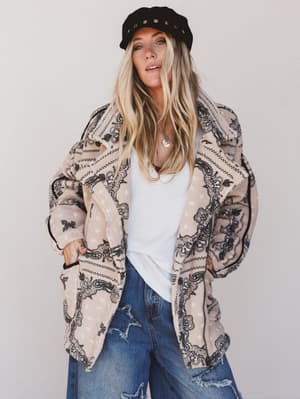 Woman wearing a patterned coat, white shirt, and jeans against a plain background