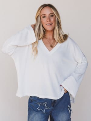 Woman wearing a white sweater and blue jeans against a plain background