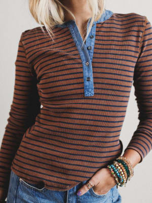 Person wearing a brown and blue striped long-sleeve shirt with denim collar.