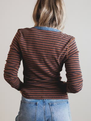 Person wearing a brown striped shirt and blue jeans against a plain background