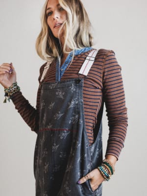 Woman wearing a striped shirt and floral overalls with a plain background