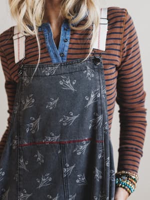 Person wearing a striped shirt and denim pinafore dress with floral pattern.