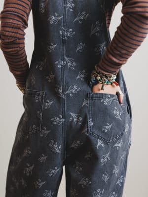 Person wearing a dark denim apron with floral patterns on a plain background