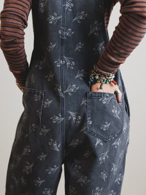 Person wearing dark denim overalls with floral patterns on a plain background